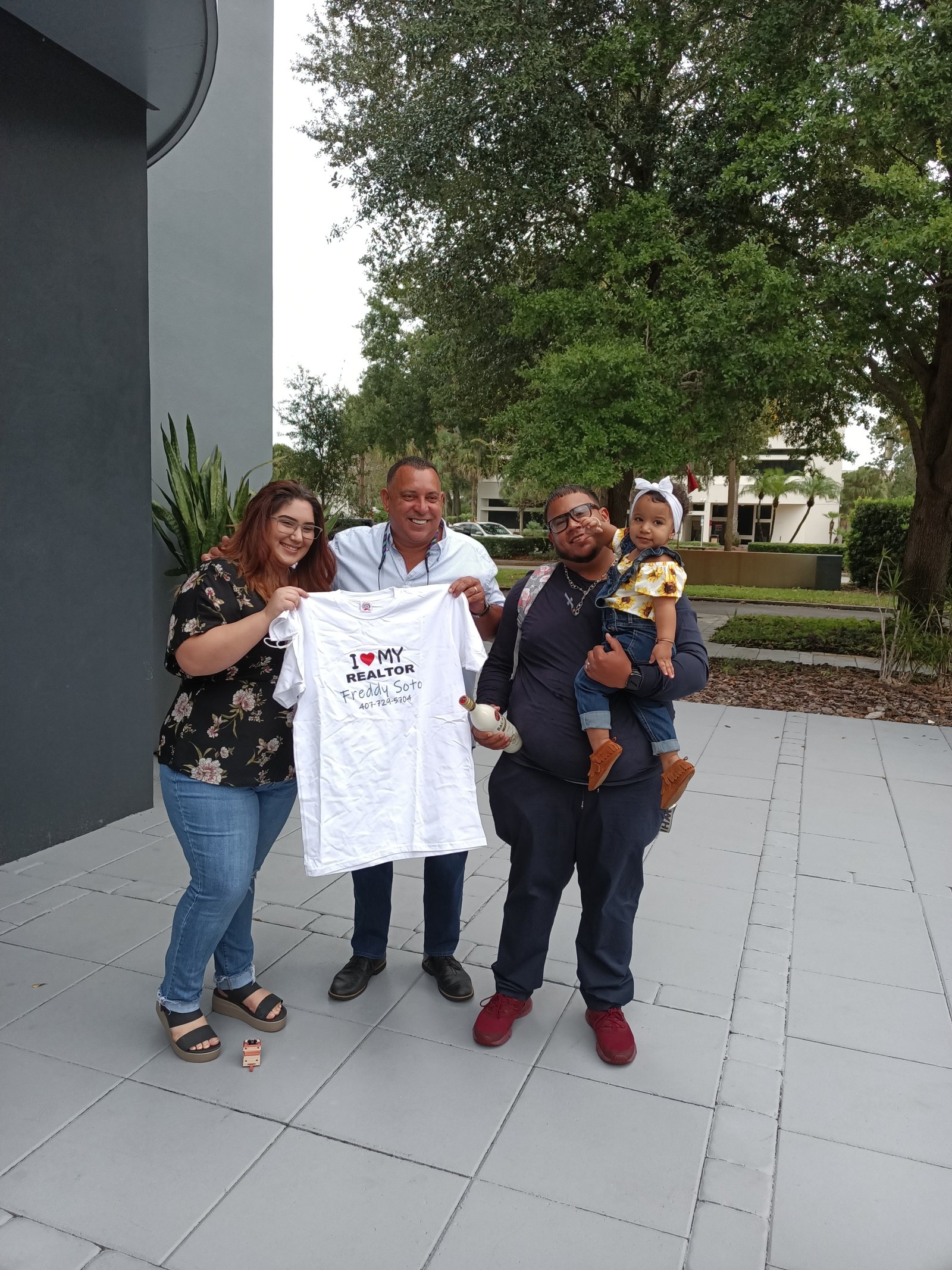 Outdoor closing celebration with a family holding a Freddy Soto real estate shirt